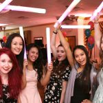 A group of girls holding up light sabers at a party.