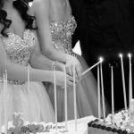 Black and white photo of two girls lighting candles on a cake.