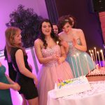 A group of women standing in front of a cake with candles.
