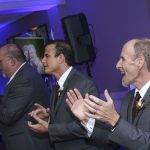 Three men in suits clapping at a wedding reception.