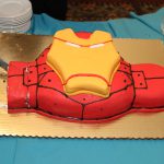 A man is cutting a cake in the shape of iron man.