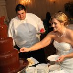 A bride and groom standing next to a chocolate fountain.