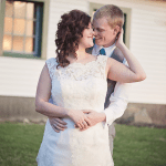 A bride and groom hugging in front of a house.