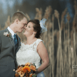 A bride and groom kissing in front of tall reeds.