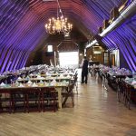 A wedding reception in a barn with tables and chairs.