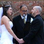 A bride and groom exchange vows in front of a brick wall.
