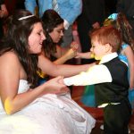 A woman in a wedding dress dancing with a little boy.