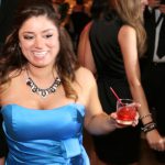 A woman in a blue dress holding a drink at a party.