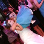 A bride is holding a little girl on the dance floor.