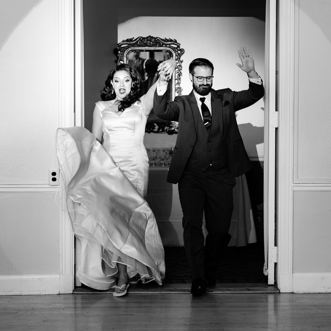 A wedding couple is walking out of a doorway.
